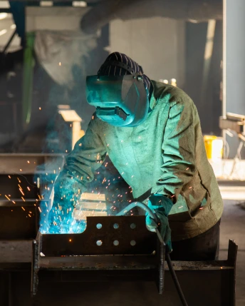 Soldador con casco realizando trabajos de soldadura en acero en una fábrica de manufacturas diversas